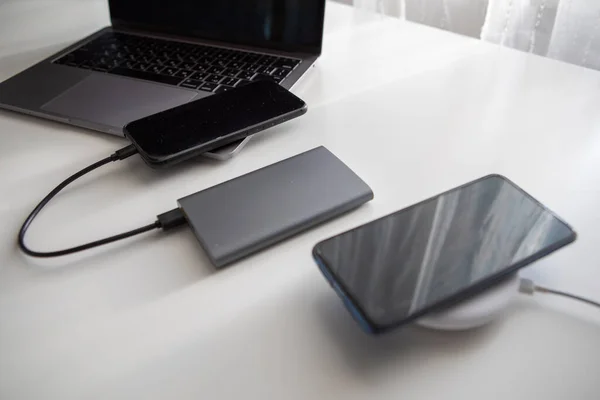 laptop with smart watch computer mouse and phone charging on wireless charger on white table