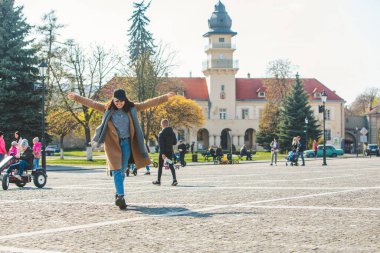 Şehir caddesinde kahverengi paltolu genç ve şık bir kadın yürüyor.