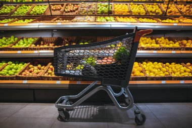 Arkadaki markette portakal ve elmalarla resim rafının ortasındaki alışveriş arabası.