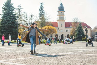 Şehir caddesinde kahverengi paltolu genç ve şık bir kadın yürüyor.