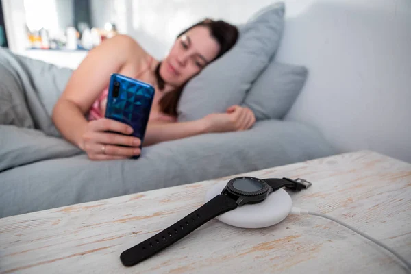 妇女在手机上上网躺在床上智能手表无线充电器复制空间 — 图库照片