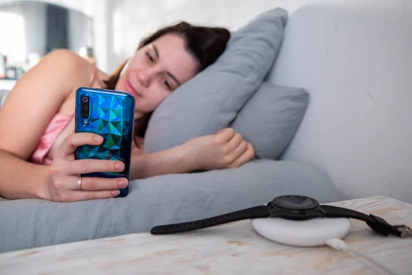 Woman Surfing Internet Cellphone Laying Bed Smart Watch Wireless Charger — Stock Photo, Image