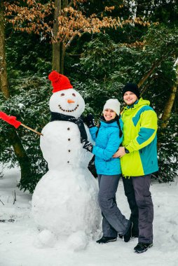 Kırmızı şapkalı kardan adamın yanında poz veren çift. kış tatili