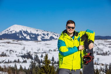 Güneş gözlüklü gülümseyen adam elinde snowboard tutuyor. Boşluğu kopyala