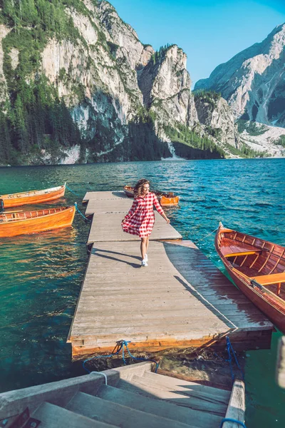 赤いドレスの木のボートで山の湖の桟橋を歩く女性 — ストック写真