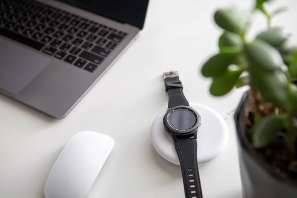 overhead view of computer mouse with laptop and smart watch on wireless charger black and white flatlay