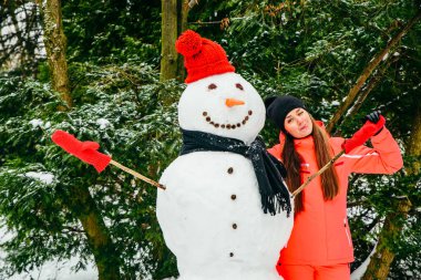 Kırmızı şapkalı ve eldivenli kardan adamla poz veren kadın. Kış tatili