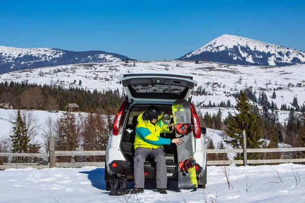 Arabanın Bagajında Oturan Adam Snowboard Için Üstünü Değiştiriyor Arkaplanda Dağlar — Stok fotoğraf