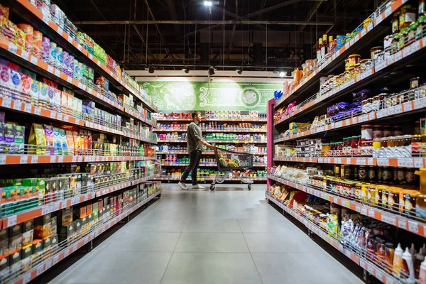 Jonge Man Met Winkelwagentje Tussen Winkel Plank Kruidenier — Stockfoto