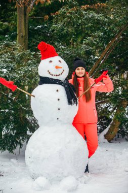 Kırmızı şapkalı ve eldivenli kardan adamla poz veren kadın. Kış tatili