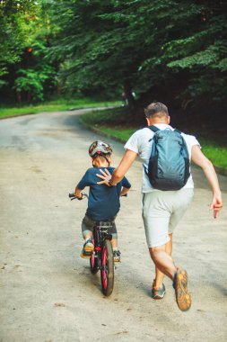 Baba oğluna bisiklet sürmeyi öğretiyor. Yaz zamanı. halka açık park