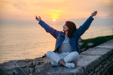 genç güzel kadın güzel gün batımı bakarak uçurumda oturan. yaz seyahat konsepti