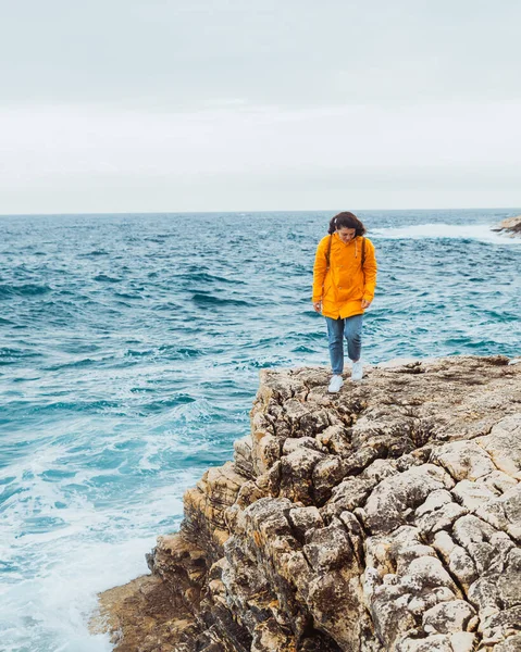 嵐の海の近くの崖を歩く黄色いレインコートの女 コピースペース — ストック写真