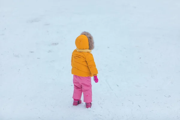 little kid in colored winter clothes yellow coat and pink pants from behind