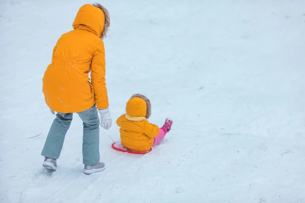 雪に覆われた丘の冬の季節から滑り込む娘を持つ母親 — ストック写真
