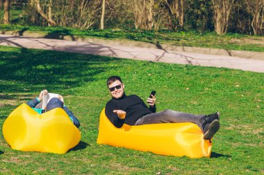 iki erkek arkadaşlar internet sörf kitapları okuma sarı şişme yatak üzerinde yatıyordu. güneşli bahar günü,