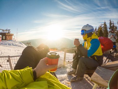 Karlı tepenin tepesinde dinlenen bir çift çay içiyor. Snowboard ve kayak. kış ekstrem spor