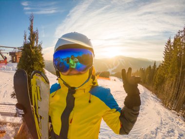 Gün batımında tepede kayakla poz veren kadın gözlükleriyle yansıyor.
