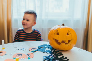 Balkabağı kafalı küçük çocuk cadılar bayramı hazırlığı yapıyor.
