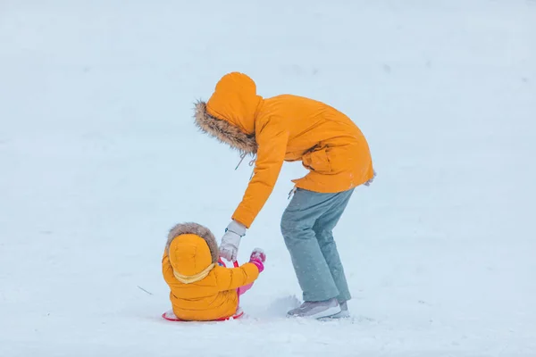 雪に覆われた丘の冬の季節から滑り込む娘を持つ母親 — ストック写真