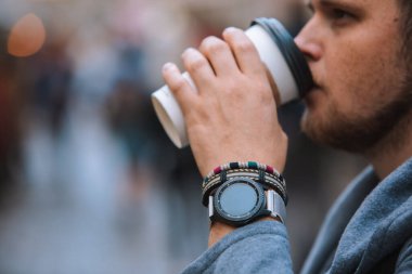 Tek kullanımlık fincandan kahve içen, bileğinde bileklik olan bir adam.