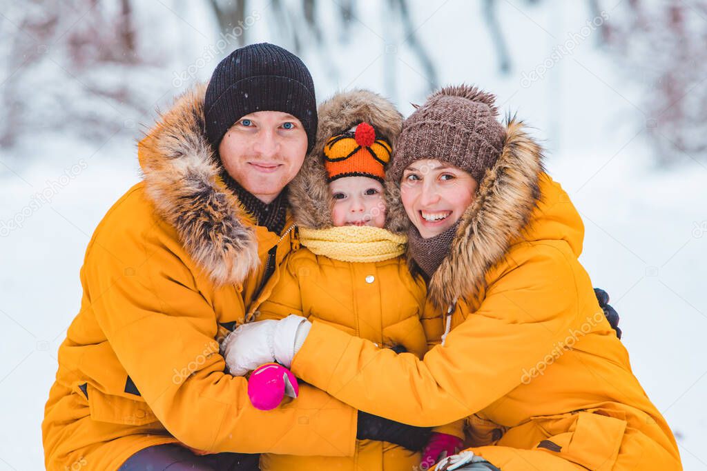 portrait of young smiling family at yellow winter coats looking at camera. mother father and little daughter
