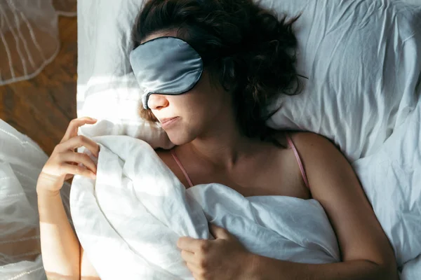 woman sleeping in mask in bed bright light on face morning time