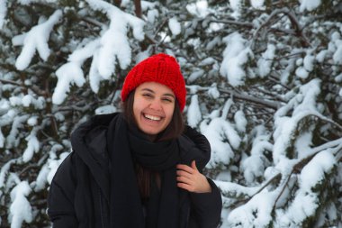 Arka planda bubo köknar ağacı olan kırmızı şapkalı, kışın gülümseyen genç kadın portresi. şık konsept