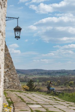 Eski kale duvarının yanında güzel manzaralı bir bankta oturan kadın. güneşli sıcak hava