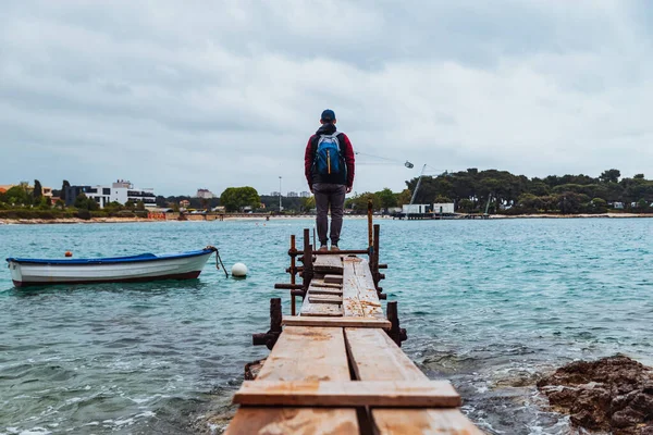 Man standing at edge of the small fishing pier looking at stormy sea —  Stock Photo © Vera_Petrunina #277727156