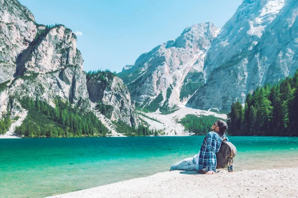 男は湖のビーチに座っているイタリアのドロマイトのバックパック山 — ストック写真