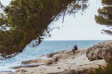 Kayalık sahilde oturmuş fırtınalı denize bakan bir adam. yaz seyahati kavramı