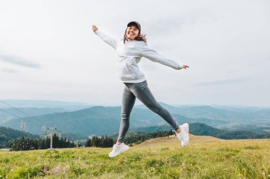 Dağın zirvesinde zıplayan kadın, arka plandaki vadi manzarası, yürüyüş konsepti.