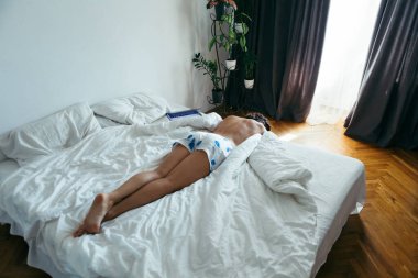 woman laying on the bed white sheets light from window with curtains. copy space