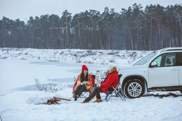 man with woman sitting on chairs near camp fire in winter time. car travel. active lifestyle