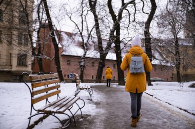Arkadan bakan kadın, karlı şehir caddesinde yürüyor.