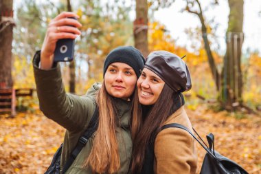 Güz parkında telefonda selfie çeken iki güzel kadın.