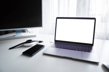 Bilgisayar fareli bir dizüstü bilgisayar ve akıllı saat beyaz masada kablosuz şarj cihazıyla şarj ediliyor
