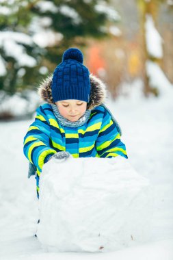 Küçük tatlı çocuk kardan adam yapıyor. Yuvarlanan büyük bir kartopu. kış tatili
