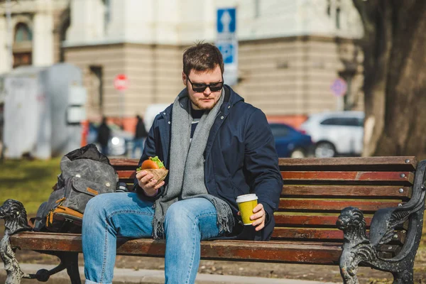 Genç Adam Yeme Hamburger Içecek Kahve Şehir Bankta Oturan Gülümsüyor — Stok fotoğraf