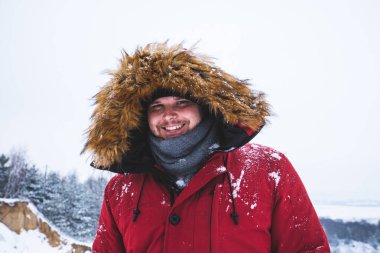 kırmızı kış ceket kürk başlık arka plan üzerinde kar alan genç adam gülümseyen.