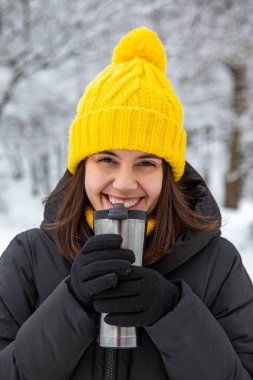Kış kıyafetli gülümseyen kadın doldurulabilir kupa fotokopi alanından sıcak bir şeyler içiyor.