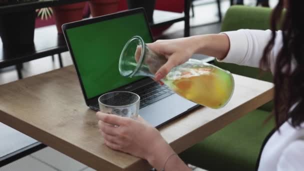 Frau gießt Orangenlimonade auf gläsernen Laptop mit grünem Bildschirm — Stockvideo