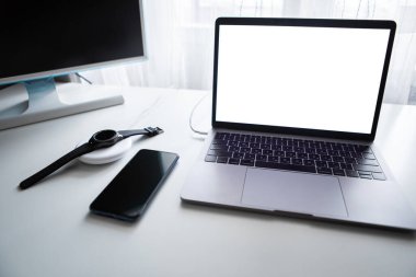 Bilgisayar fareli bir dizüstü bilgisayar ve akıllı saat beyaz masada kablosuz şarj cihazıyla şarj ediliyor