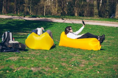 çift şehir parkında sarı şişme yatak üzerinde yatıyordu. kitap okuma. selfie çekiyor. boş zaman