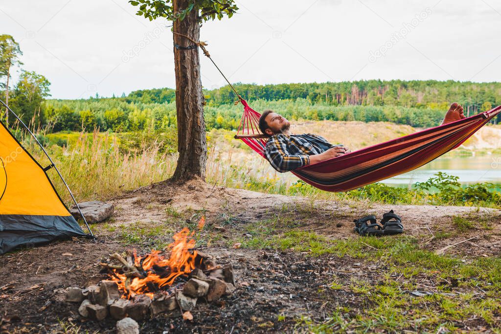 man laying on hammock at lake beach near camp fire tourism concept