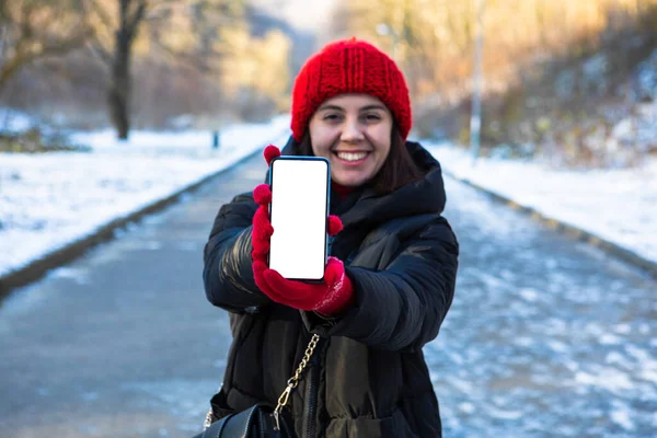 Молодая Улыбающаяся Женщина Зимнем Наряде Держит Телефон Белым Пустым Пустым — стоковое фото
