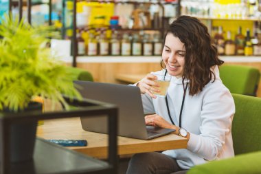 Genç ve güzel bir kadın laptopta çalışıyor, kafede limonata içiyor.