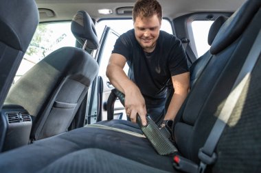 Adam elektrikli süpürge koltuklarıyla arabanın içini temizliyor.