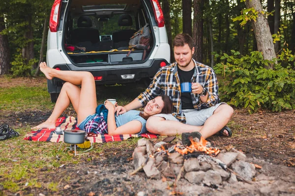 couple sitting on blanket near bonfire white suv vehicle on background hiking concept